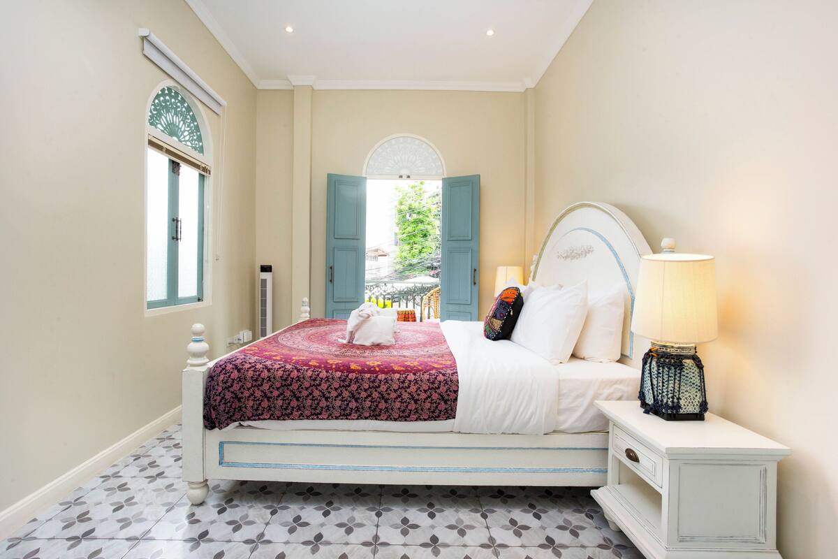 A neatly arranged bedroom with a bed, a bedside table with a lamp, and a view through an open door.