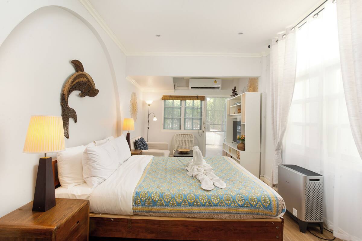 A neatly arranged bedroom with a bed, bedside lamp, and a large window with curtains.