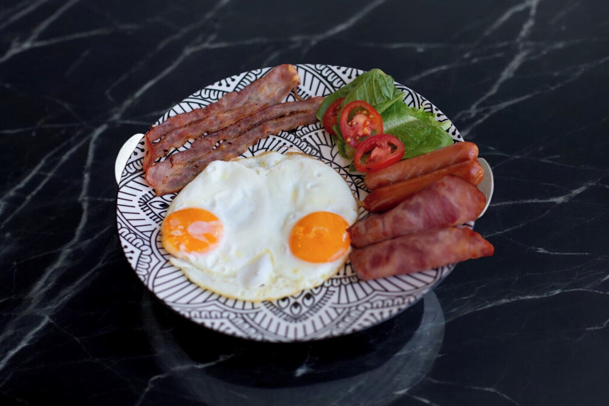 Un plat amb bacon, ous i verdures sobre un plat estampat.
