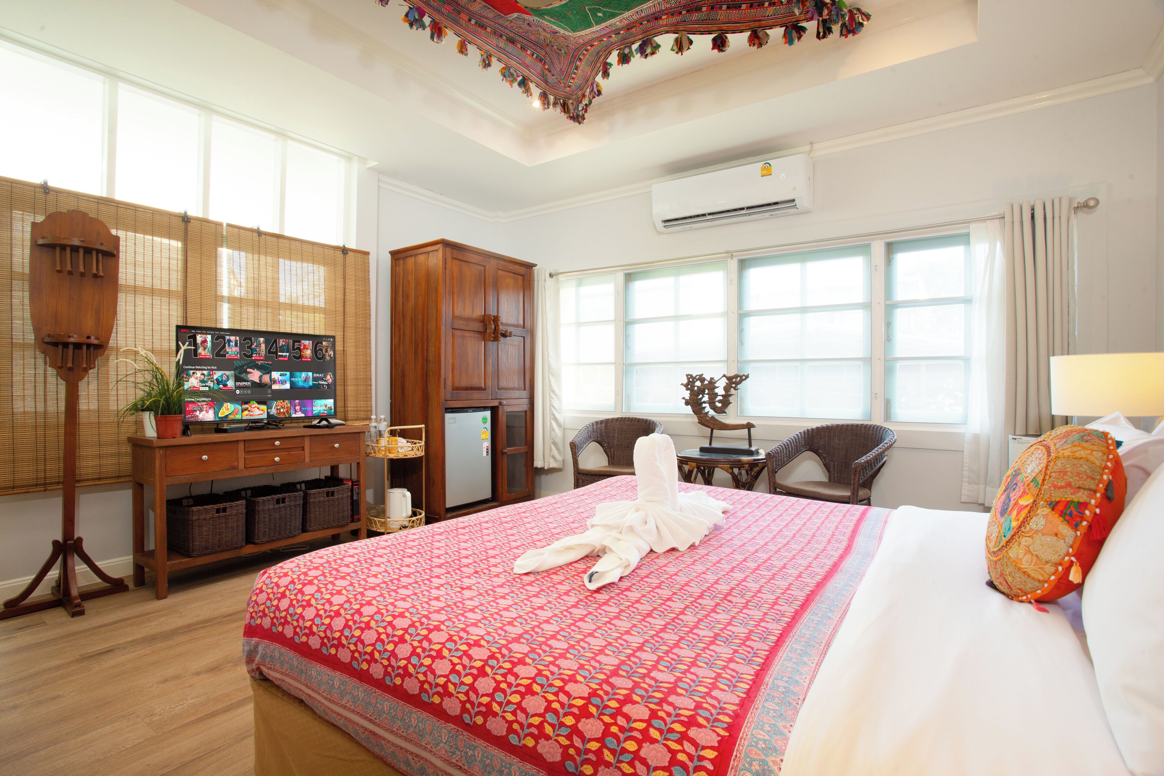 Habitación de hotel con una cama grande, un escritorio de madera con una computadora, una mesita con una silla y una ventana con cortinas.