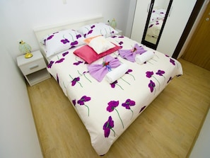 A neatly made bed with floral bedding, a bedside table with a lamp, and a mirror on the wall.