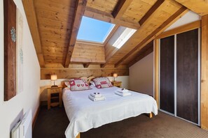 A bedroom with a sloped ceiling, a skylight, a bed with white bedding, two bedside tables with lamps, and a large sliding door.