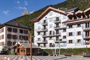 A multi-story hotel with balconies, a mountain view, and a wooden cabin.