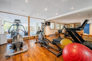 A gym with exercise equipment, large windows, and wooden flooring.