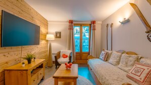A cozy room with a wooden wall, a bed with white bedding, a small table with a plant, and a TV mounted on the wall. - V Loriaz 14: Beside Ski Lift; Pool, Sauna & Gym, Vallorcine (Argentiere), France (Vallorcine (Argentiere))
