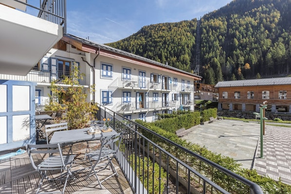 Un hotel con posti a sedere all'aperto, un balcone e lo sfondo di una montagna.