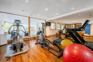 A gym with exercise equipment, large windows, and wooden flooring.