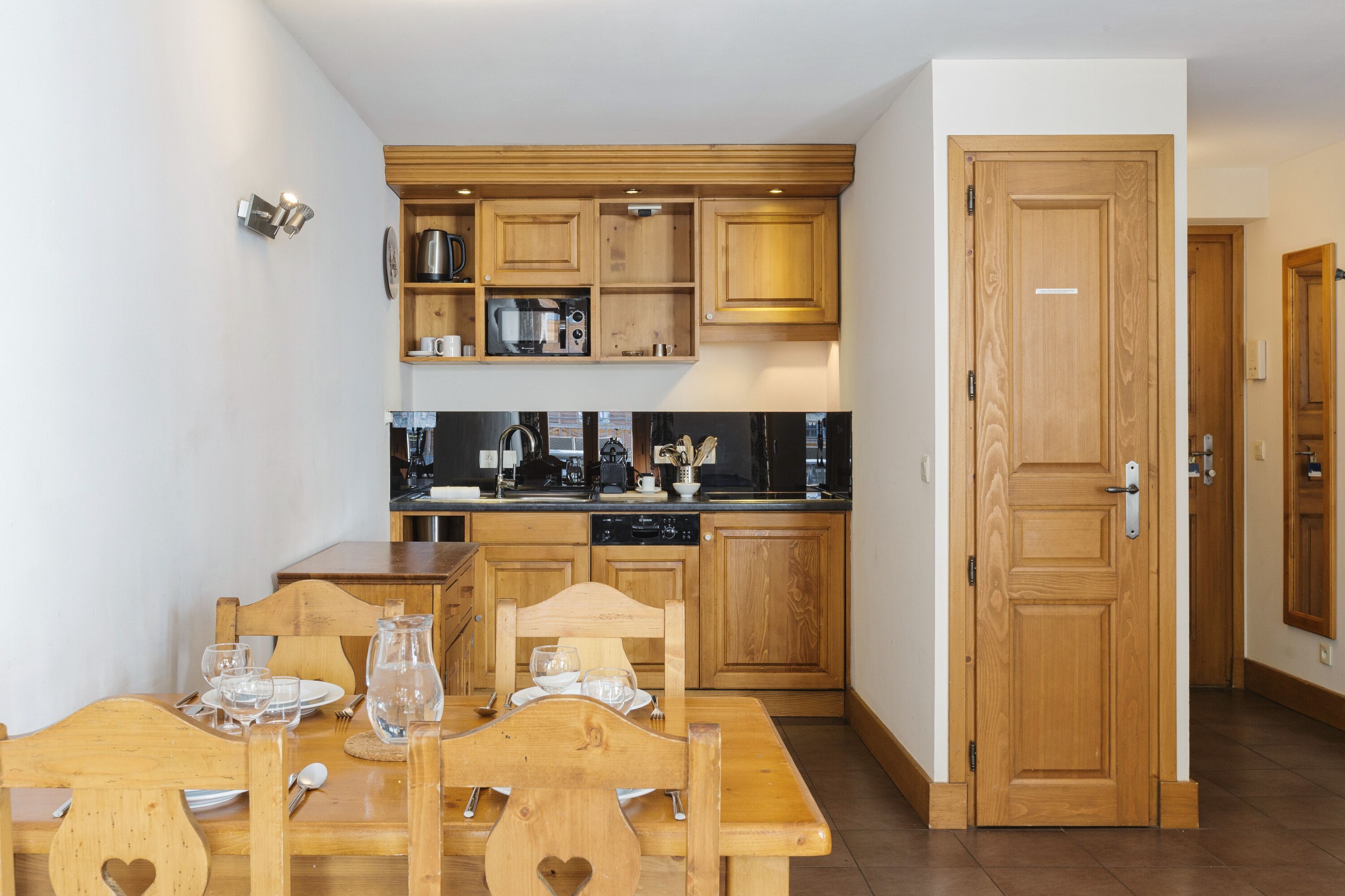 Cocina compacta con armarios de madera y comedor con una mesa preparada para dos.