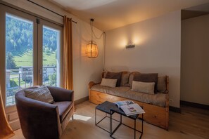 Una habitación acogedora con un sofá, una silla, una mesa con una revista y un ventanal con cortinas.