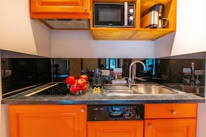 Uma cozinha com armários cor de laranja, uma lava-louças Bosch, um micro-ondas e uma cafeteira em uma prateleira de madeira.
