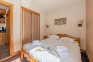 Una cama bien hecha con sábanas y toallas blancas, un cabecero de madera y una mesita de noche con una lámpara.