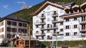 A multi-story hotel with balconies, a mountain view, and a wooden cabin.