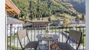 A balcony with wicker chairs, a table with a vase, and a view of a mountain and buildings.