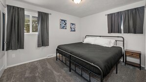 Een slaapkamer met een bed met metalen frame, een nachtkastje en een raam met gordijnen.