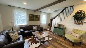 Un salon avec un canapé en cuir marron, un fauteuil vert, une table basse en bois et un escalier avec une rampe en bois.
