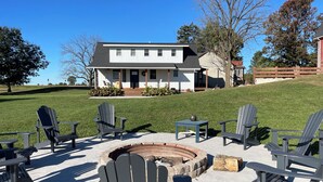 Une maison avec un foyer extérieur et des fauteuils Adirondack dans le jardin.