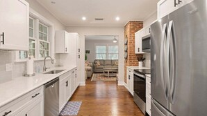 A modern kitchen with white cabinetry, a stainless steel refrigerator, and a wooden floor. - House is close to Beach Pier, Shops & Restaurants (Saint Simons Island)