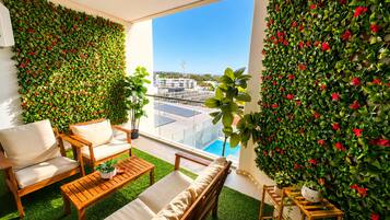 Un balcón con vistas a una piscina y edificios, amueblado con sillas de madera y una pequeña mesa.