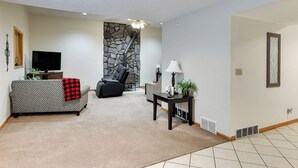 A living room with a stone fireplace, a sofa, a television, and a lamp. - Aksarben Two Bed, One Bath Duplex Suite (Omaha)