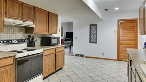 A kitchen with wooden cabinets, a stove, a microwave, and a tiled floor. - Aksarben Two Bed, One Bath Duplex Suite (Omaha)