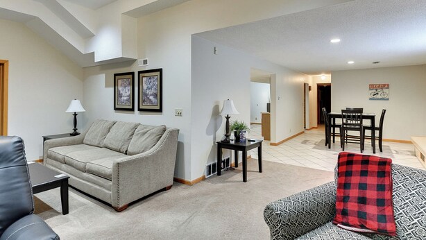 A living room with a sofa, a coffee table, a dining table with chairs, and a lamp. - Aksarben Two Bed, One Bath Duplex Suite (Omaha)
