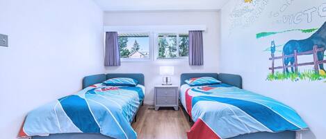 A room with two beds, a window with curtains, a radiator, and a wall mural.