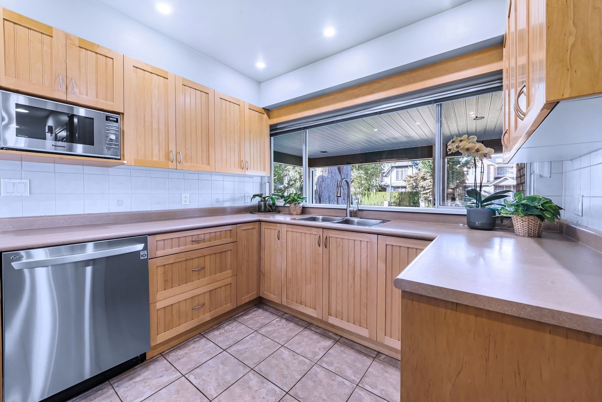 A modern kitchen with wooden cabinets, a stainless steel microwave, a dishwasher, and a window with a view of the outside.