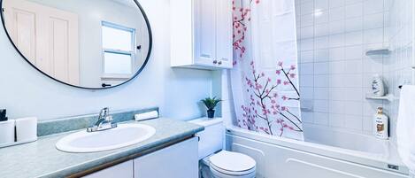 A modern bathroom with a round mirror, white cabinets, a sink, a toilet, and a shower with a floral shower curtain.