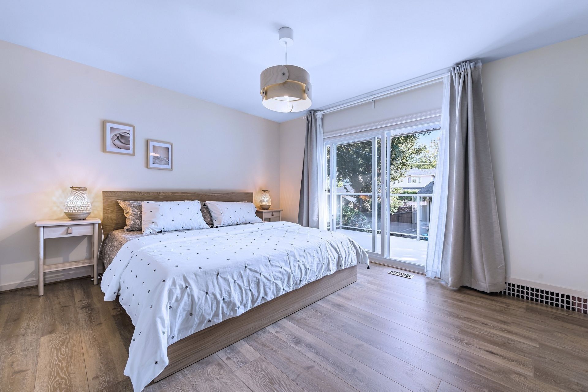 A bedroom with a large bed, wooden flooring, a window with curtains, and a ceiling light.