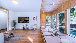 Ein modernes Wohnzimmer mit Holzboden, einem großen Fenster, einer Couch, einem Sessel und einem kleinen Tisch mit Pflanzen.