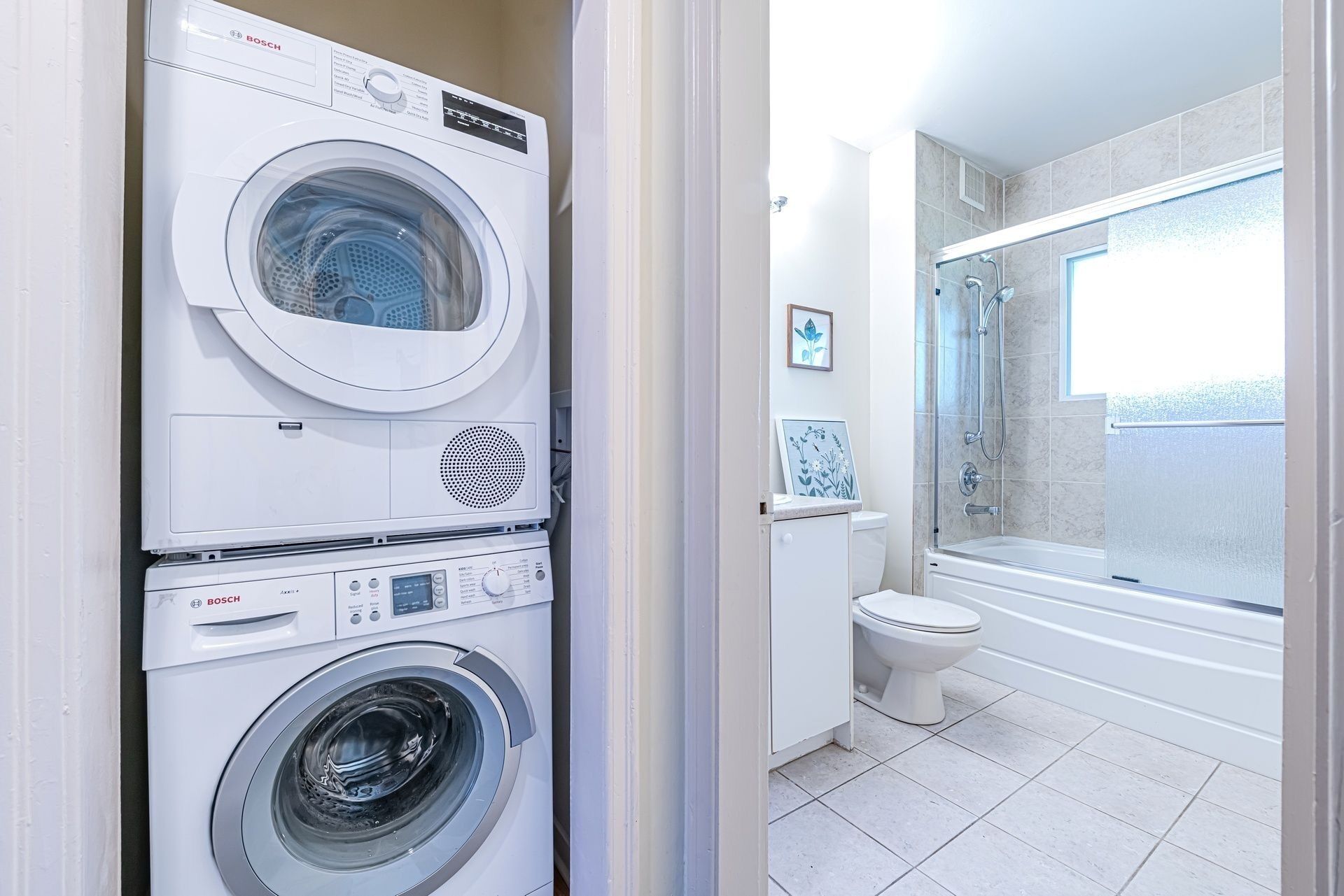 A laundry area with a Bosch washing machine and dryer, a toilet, and a shower in a bathroom.