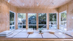 Ein Zimmer mit Tatami-Matten, Holzböden und großen Fenstern mit Blick auf Häuser.