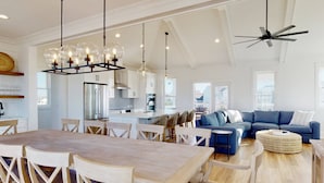 A spacious living area with a dining table, blue sofa, and a ceiling fan.