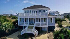 A two-story beachfront house with a balcony and a staircase leading to the upper level.