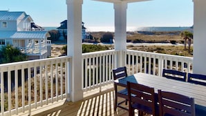 A covered outdoor area with a table and chairs, overlooking a beach and ocean.