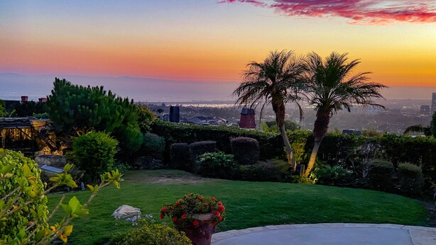 Um jardim paisagístico com piscina, vasos de plantas e vista para o horizonte urbano ao pôr do sol.