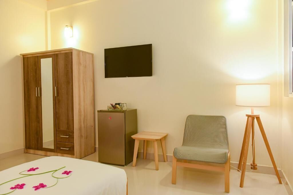 Une chambre d’hôtel comprenant un lit, une armoire en bois, une petite table, une chaise, un bureau, une lampe et un téléviseur à écran plat.
