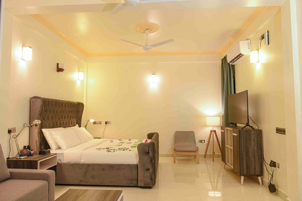 A hotel room with a bed, a desk, a chair, a TV, and a wardrobe.