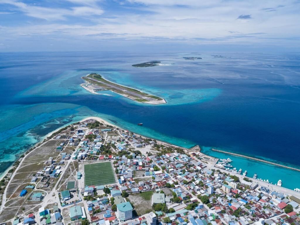 An aerial view of a coastal town with a marina, clear blue waters, and a small island with a runway.