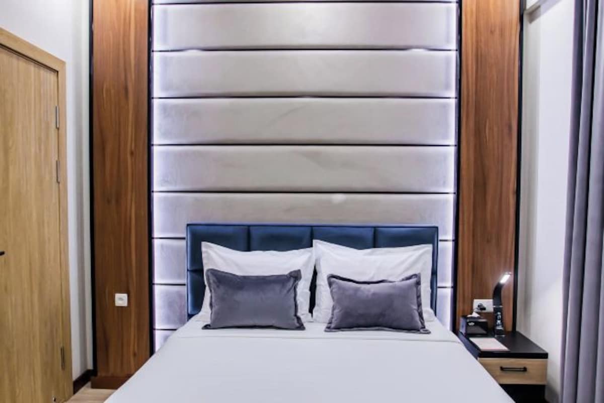 A bedroom with a large bed, a wooden wardrobe, and a modern headboard.