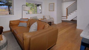 A living room with a brown leather sofa, a wooden coffee table, and a staircase leading to an upper level. - Hidden Gem, Hot tub, Garage, Amazing Views! (Mt. Crested Butte)