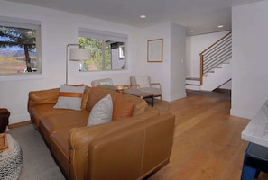 A living room with a brown leather sofa, a wooden coffee table, and a staircase leading to an upper level. - Hidden Gem, Hot tub, Garage, Amazing Views! (Mt. Crested Butte)