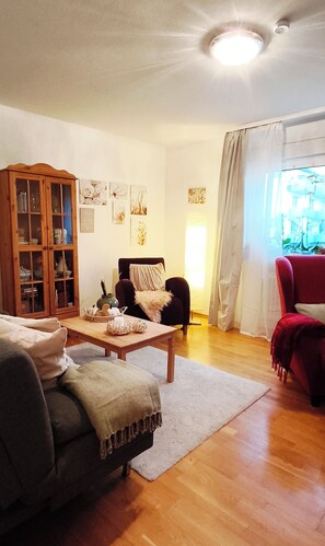 Ein Wohnzimmer mit einem Holzkabinett, einer Couch, einem roten Sessel und einem Tisch mit Dekoration.