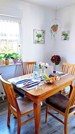 A dining area with a wooden table, chairs, and a window with plants. - Vacation apartment Sartorius, Holiday apartment am Hemsberg (Bensheim)