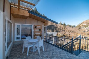 A balcony with a table and chairs, a wooden slatted wall, and a view of a hilly landscape. - Jomotel Dayaar (Theog)