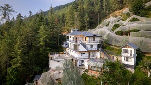 A multi-story building with balconies, surrounded by dense forest and a large net structure. - Jomotel Dayaar (Theog)