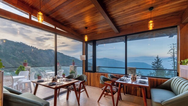 A dining area with wooden furniture and large windows offering a mountain view. - Jomotel Dayaar (Theog)