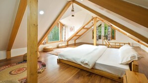 A cozy attic bedroom with a wooden bed, a colorful rug, and a view of greenery through the windows. - Jomotel Dayaar (Theog)