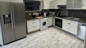 Una cocina moderna con electrodomésticos de acero inoxidable, armarios blancos y piso de baldosas.