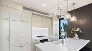 Una cocina moderna con armarios blancos, encimera de mármol e iluminación colgante.